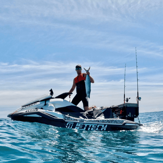Person on a jet ski holding a fish with clear blue sky and ocean background