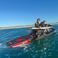 Two people on a jet ski with a surfboard in the water