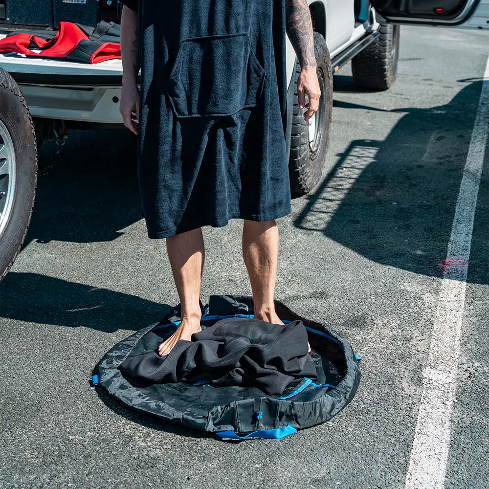 Person standing on a black round mat in a parking lot with vehicles in the background.