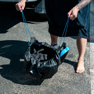 Person pulling a black bag with blue handles on a paved surface
