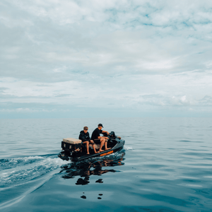 Two people on a small boat in the middle of a calm body of water with a cloudy sky.