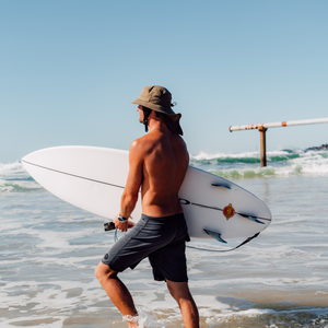 man holding surfboard wearing surf hat