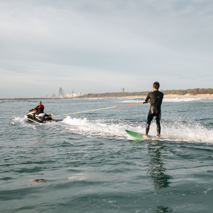 man on surfboard getting towed behind jet ski 